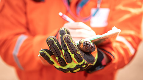 A close view of a person in PPE writing on a clipboard