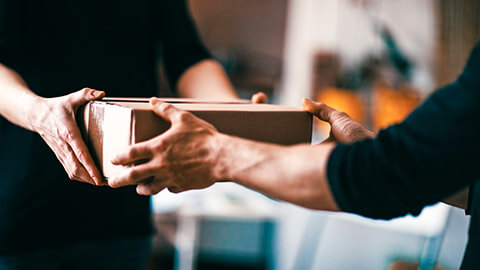 A person handing a packaged product to their colleague, for them to continue to process during delivery