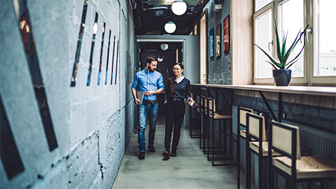 Two people making their way down a hallway in their office, while discussing an inspired idea