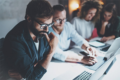 A business owner reading a document intently while partners hold a conversation in the background