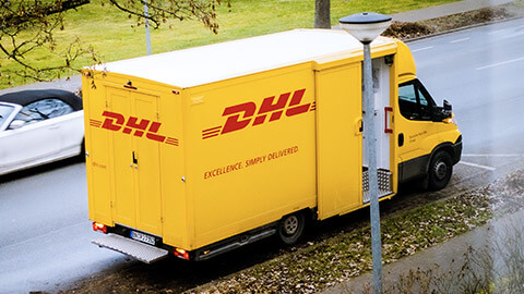 A DHL van parked on the side of the road while its driver delivers a package to a customer