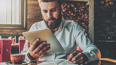 A hipster businessman reading an article on a tablet device and jotting notes