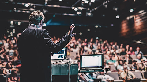 Rear wide view of a business professional giving a presentation to a large audience