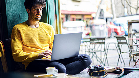 A student seated at a cafe, typing out notes on their laptop