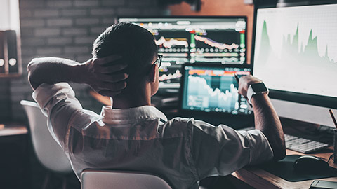 A rear view of a financial analyst checking stock movement on multiple screens