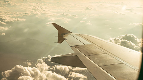 The wing of an aircraft above the clouds, with mountains down below