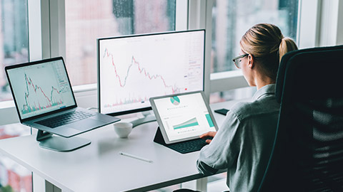 Over the shoulder view of a data analyst looking at information on 3 different screens in an office