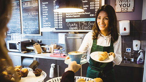 A smiling business owner handing a latte to a customer