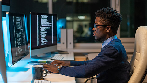 Young it-engineer of African ethnicity working with coded data while sitting in armchair in front of computer in office