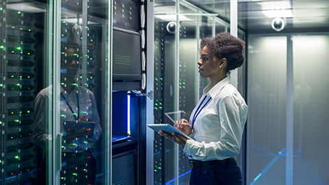 female technician working on a tablet in a data center full of rack servers running diagnostics and maintenance on the system