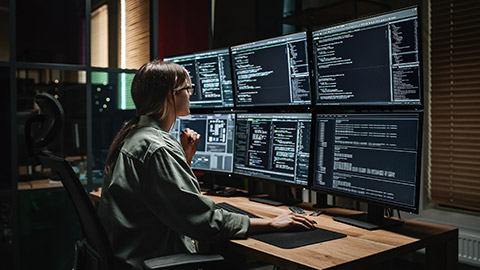 female programmer watching code languages on multiple computer screens