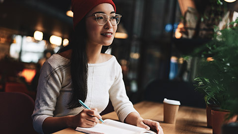 A person sitting at a desk reflecting on an event and writing notes in a notepad