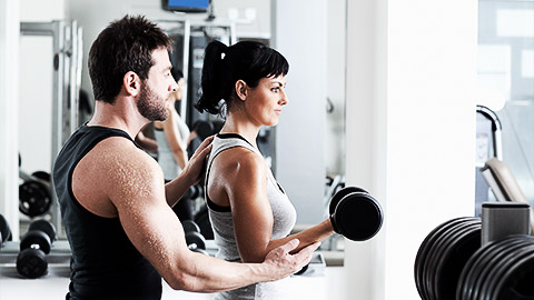 A person doing dumbbell curls while being guided closely by a trainer