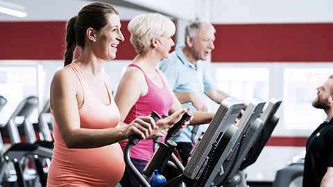 Pregnant woman and seniors training on cross trainer at the gym