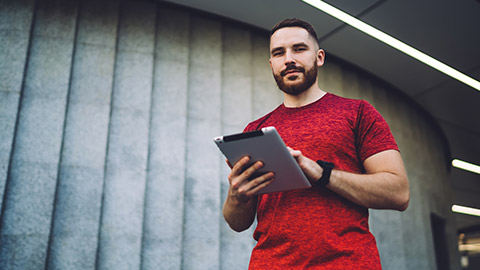 A personal trainer standing outside a gym while holding a tablet device