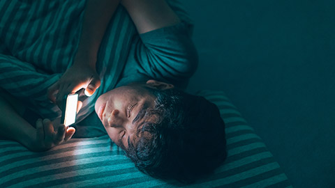 Sleepy tired teenage man under the blanket using smartphone