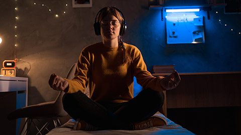 Young woman meditating, female student doing yoga and relaxation exercise on bed