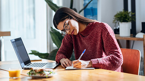 woman working with laptop while writting some notes in the kitchen at home