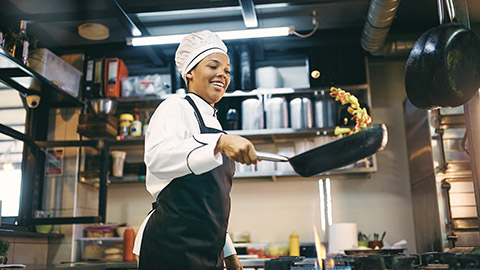 African American female chef having fun while preparing food in the kitchen at restaurant.