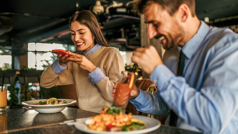 A smiling couple sitting in the restaurant and taking a photos of their meals