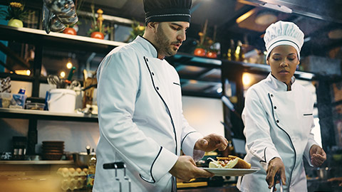 African American chef and her coworkers preparing food in the kitchen at restaurant.