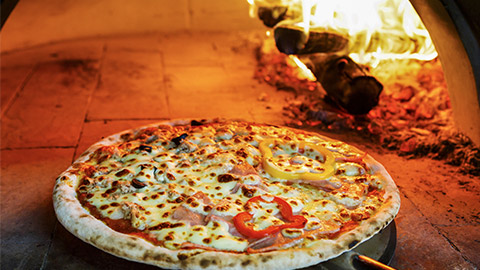 Close up pizza in firewood oven with flame behind