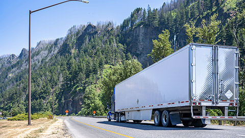 Classic blue long haul big rig semi truck tractor with chrome exhaust pipes transporting commercial cargo in refrigerator semi trailer moving on the highway road in Columbia Gorge National Reserve