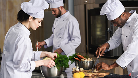 Multiracial team of cooks cooking by kitchen stove in restaurant