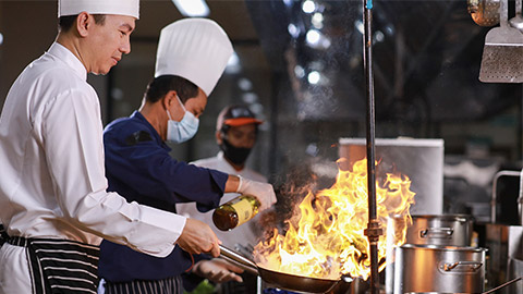 Closeup chef hands cook food with fire. Chef man burn food at professional kitchen