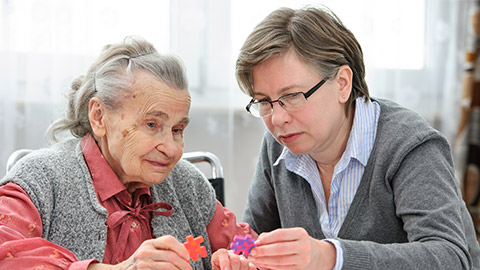 Elder care nurse playing jigsaw puzzle with senior woman in nursing home