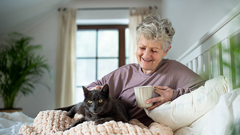 Happy senior woman with cat resting in bed at home.