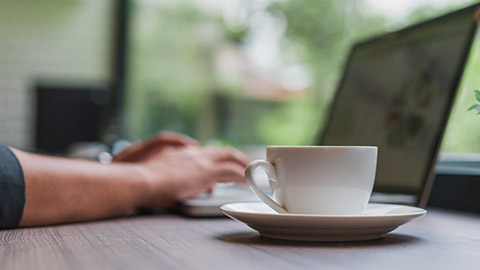 Working outside with cup and laptop computer on table.