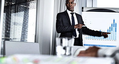 Young businessman pointing towards graph while giving presentation in office
    