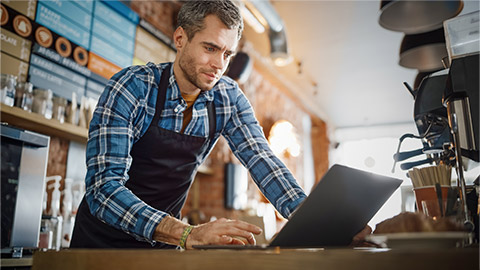 Young and Handsome Coffee Shop Owner is Working on Laptop