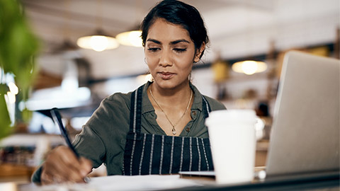 Small business owner working on a budget in her coffee shop and writing a list of stock to order.