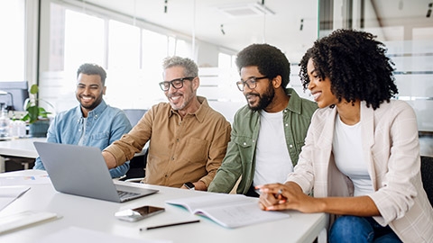 A team of professionals shares a cheerful moment around a laptop, signifying a successful collaboration and productive work environment