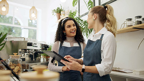 Woman, cafe and employees talking with tablet, happy and laughing in conversation or learning with new staff