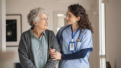 Young caregiver helping senior woman walking. Nurse assisting her old woman patient at nursing home