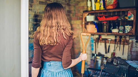 A young woman is standing in a shed holding a spade