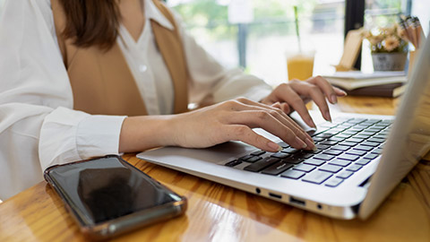 shot of woman hands typing on laptop keyboard while sitting at the table in office