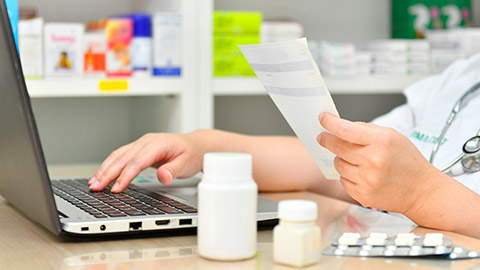 A pharmacist entering medicine details on a laptop