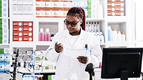 A smiling pharmacist looking at a bottle of medicine