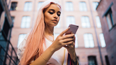 A young person standing outside looking their phone