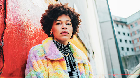 A portrait of a serious young female standing near a colourfully painted wall