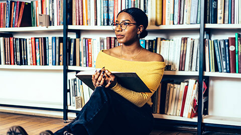 A student seated in the library, reflecting on the book they are absorbing