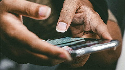 A young man sitting down, taking notes on his smartphone