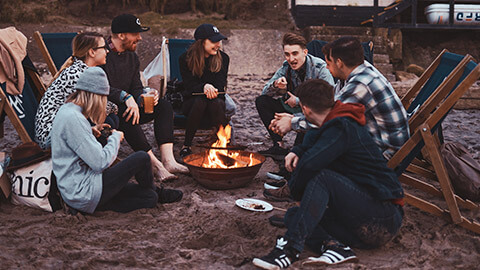 A group of people sitting around a fire on a beach listening to one person telling a story