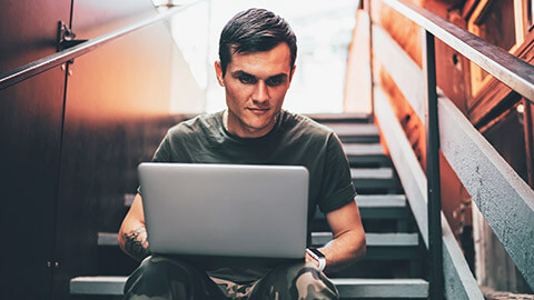 A youth worker typing a journal entry on a laptop while sitting in an outdoor environment