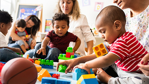 a couple of educators playing with children on the floor with toys around them