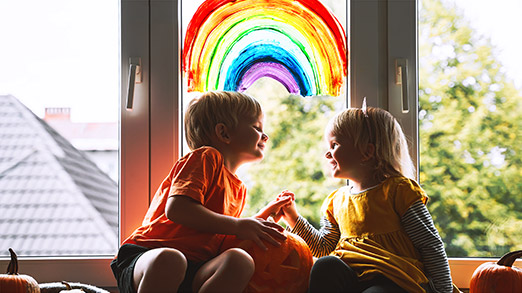 teo children sitting happily by a window with a rainbow artwork